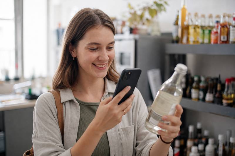 Fröhliche Person hält eine Getränkeflasche und scannt den Barcode mit dem Smartphone.
